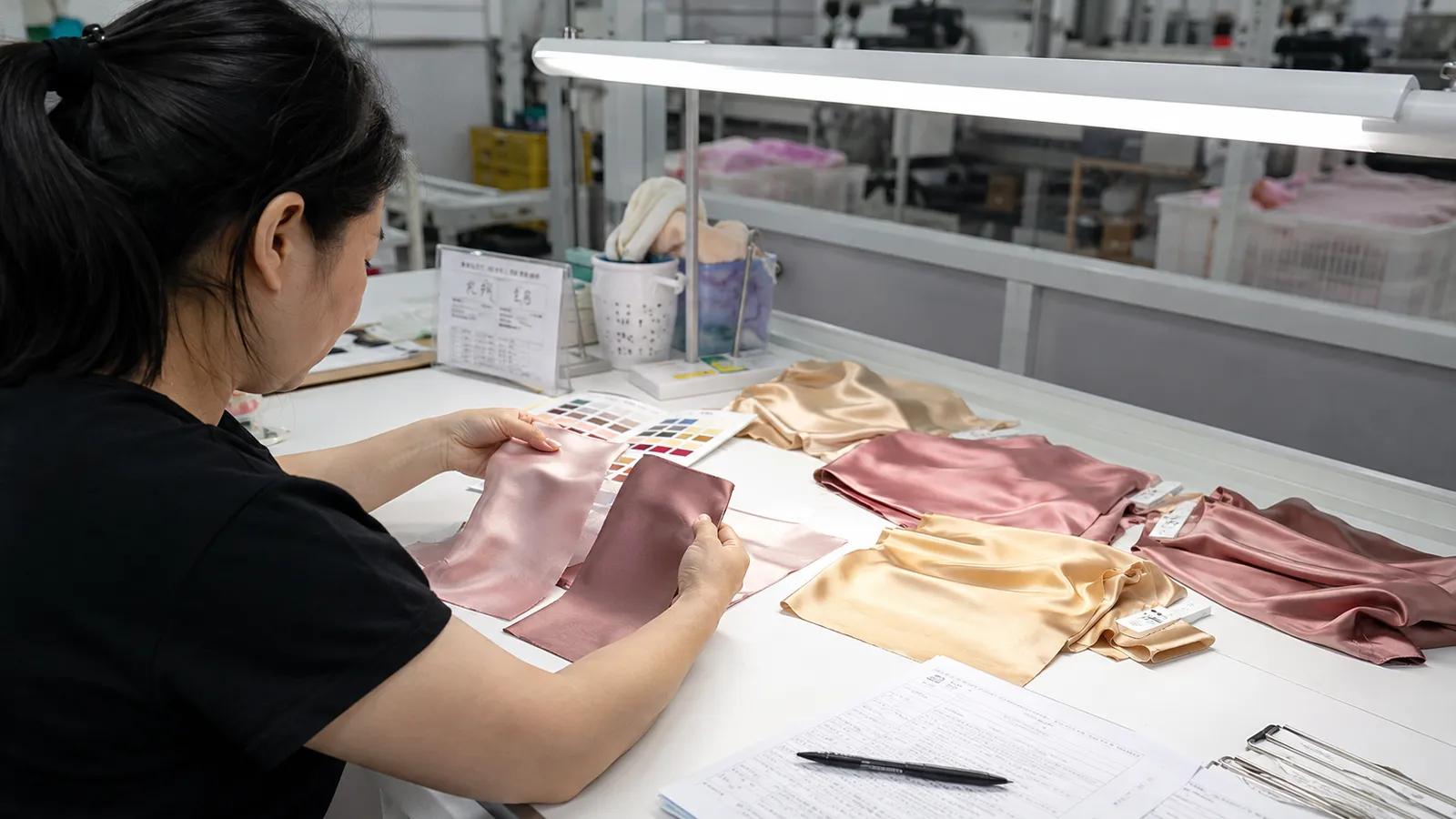 Incoming silk fabric and trim color review under inspection light to support consistent quality for B2B private label silk orders