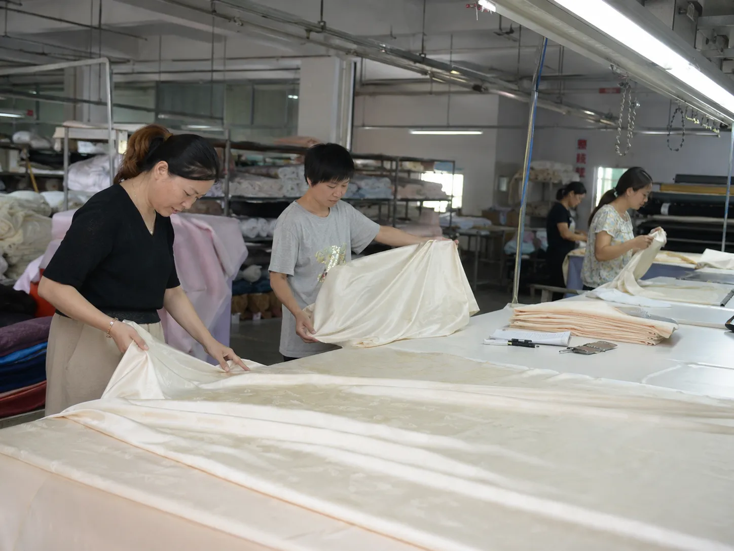 Incoming silk fabric inspection with staff reviewing material on a factory table to support consistent quality for B2B private label silk orders