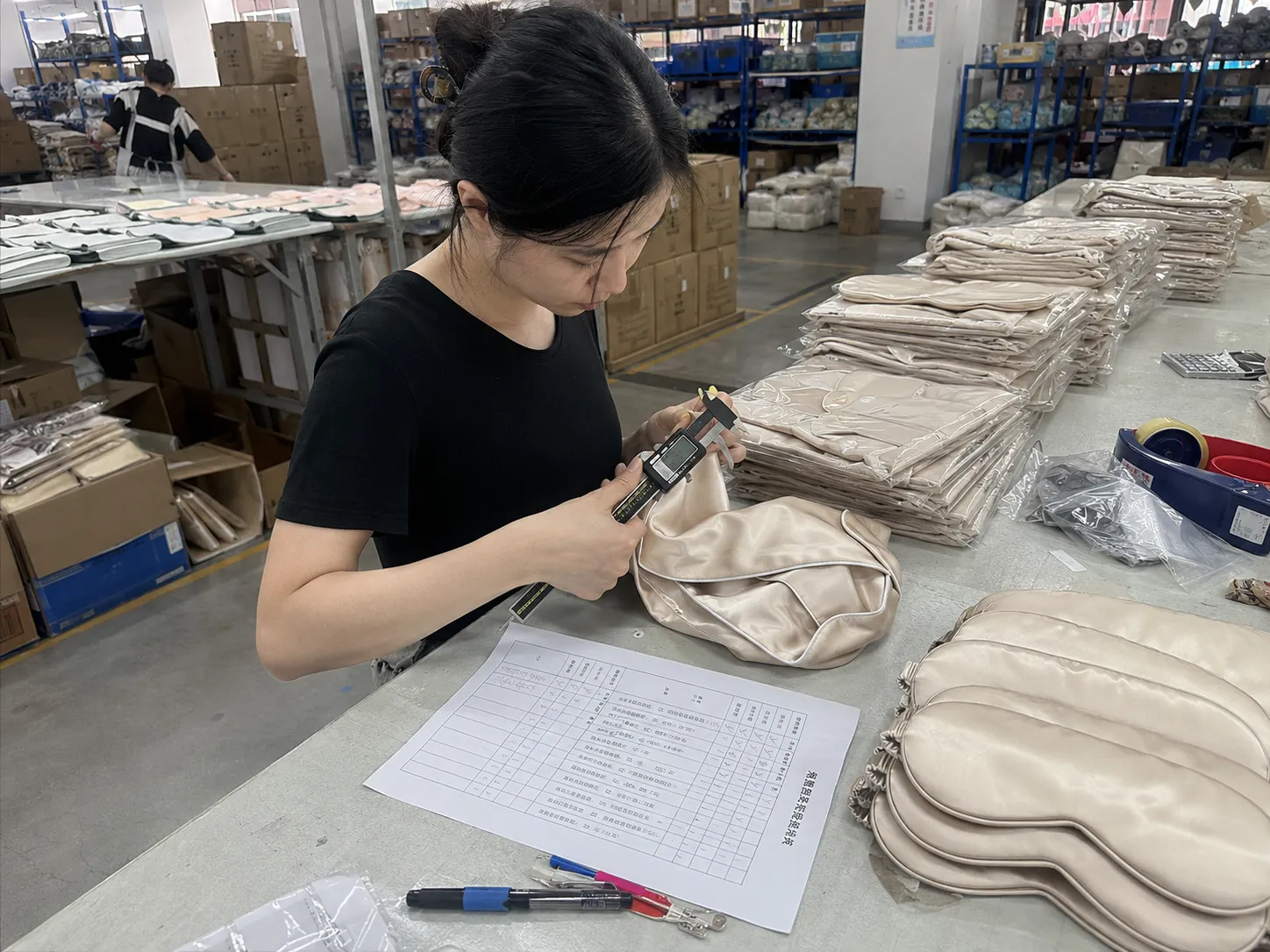 Final inspection before packing at a private label silk manufacturer, with a technician measuring silk eye mask details using calipers to support