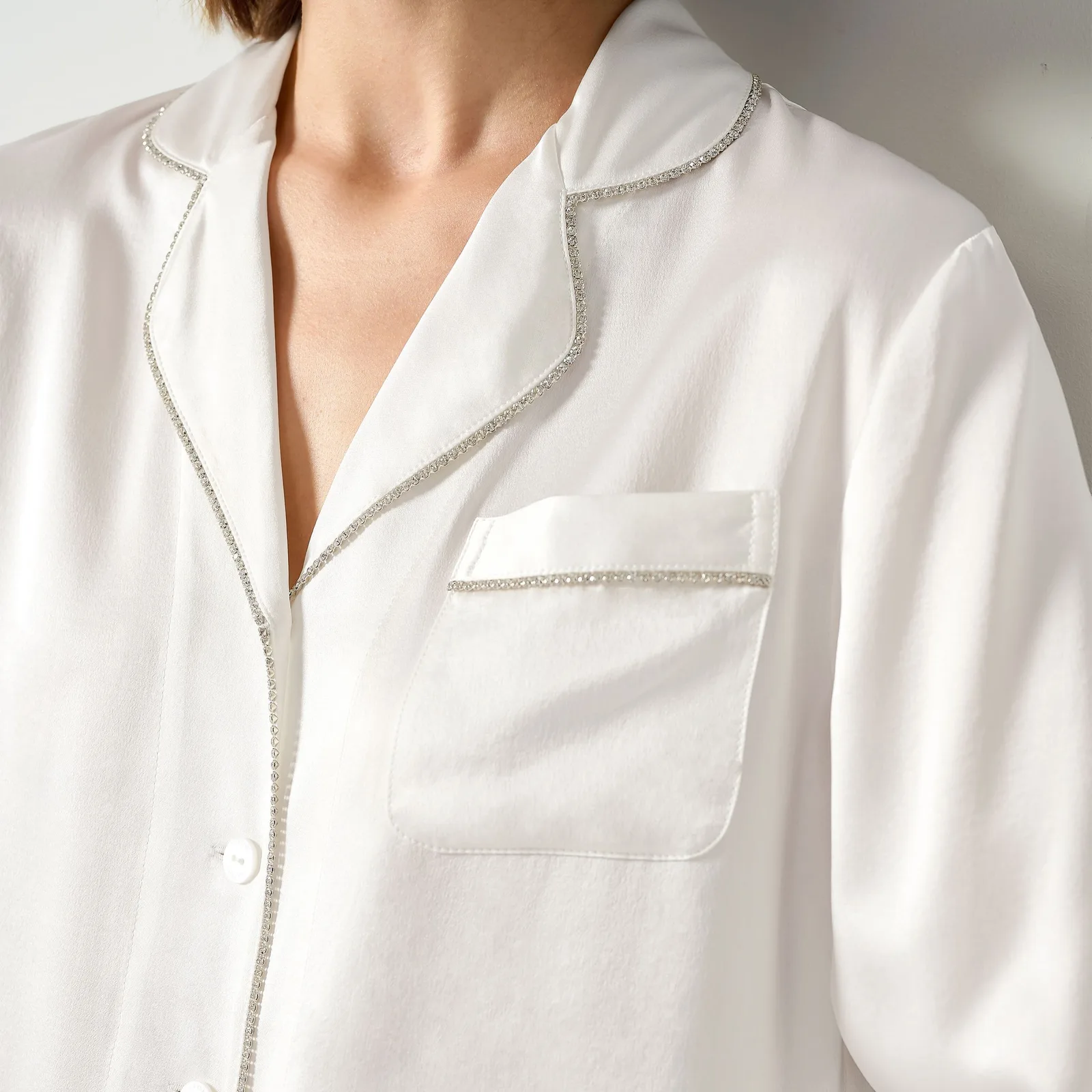 Detail view of a white private label pajama top with embellished piping, lapel collar, and chest pocket for premium sleepwear gift set programs