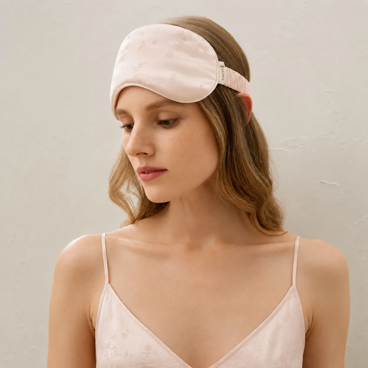 Pale pink custom silk sleep mask style with subtle floral pattern for private label beauty, spa, travel, and gift set programs