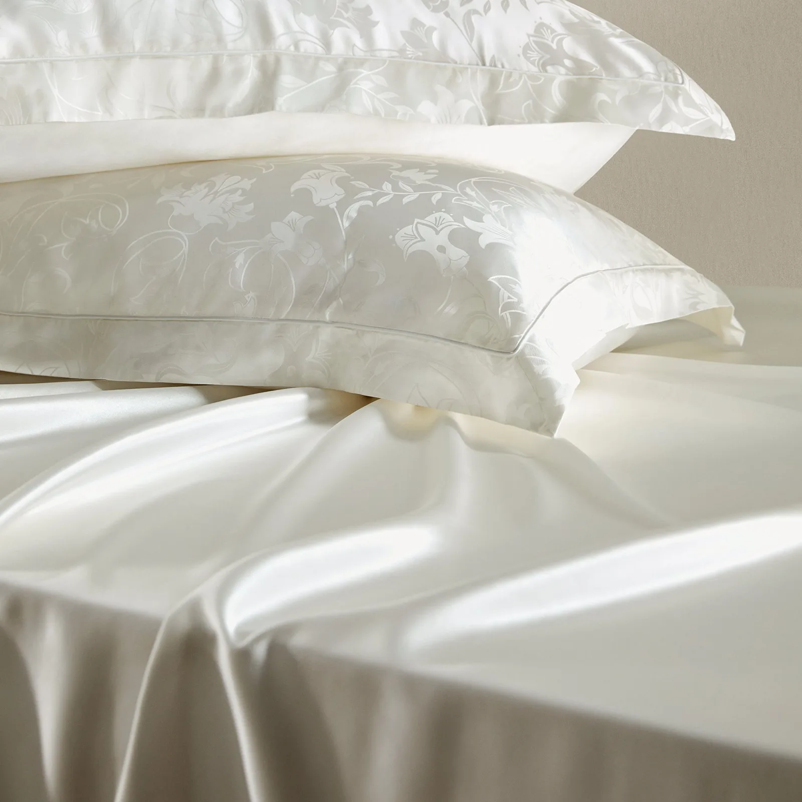 Detail view of custom silk bedding with ivory floral jacquard pillowcases and smooth sheet styling for private label bedding collections