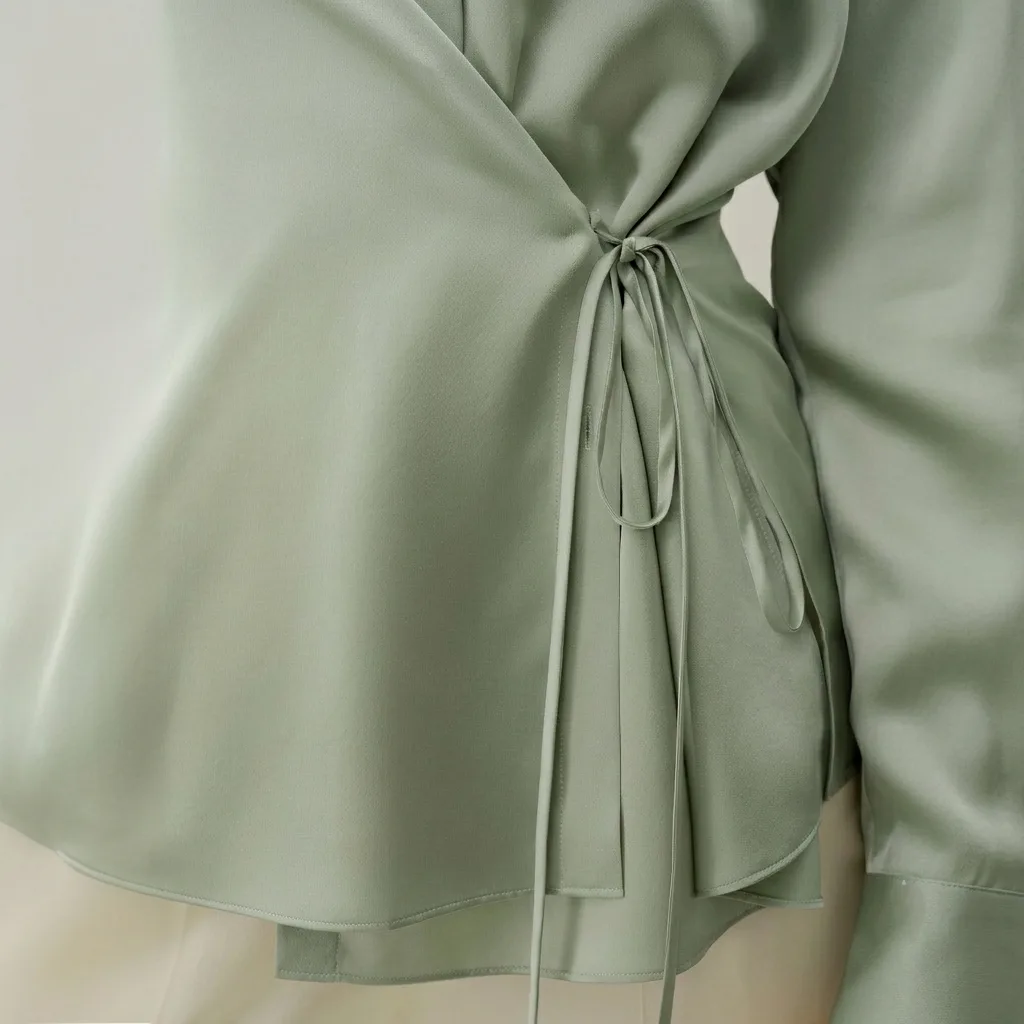 Detail view of sage green wrap-style silk blouse with side tie waist for private label custom silk clothing development