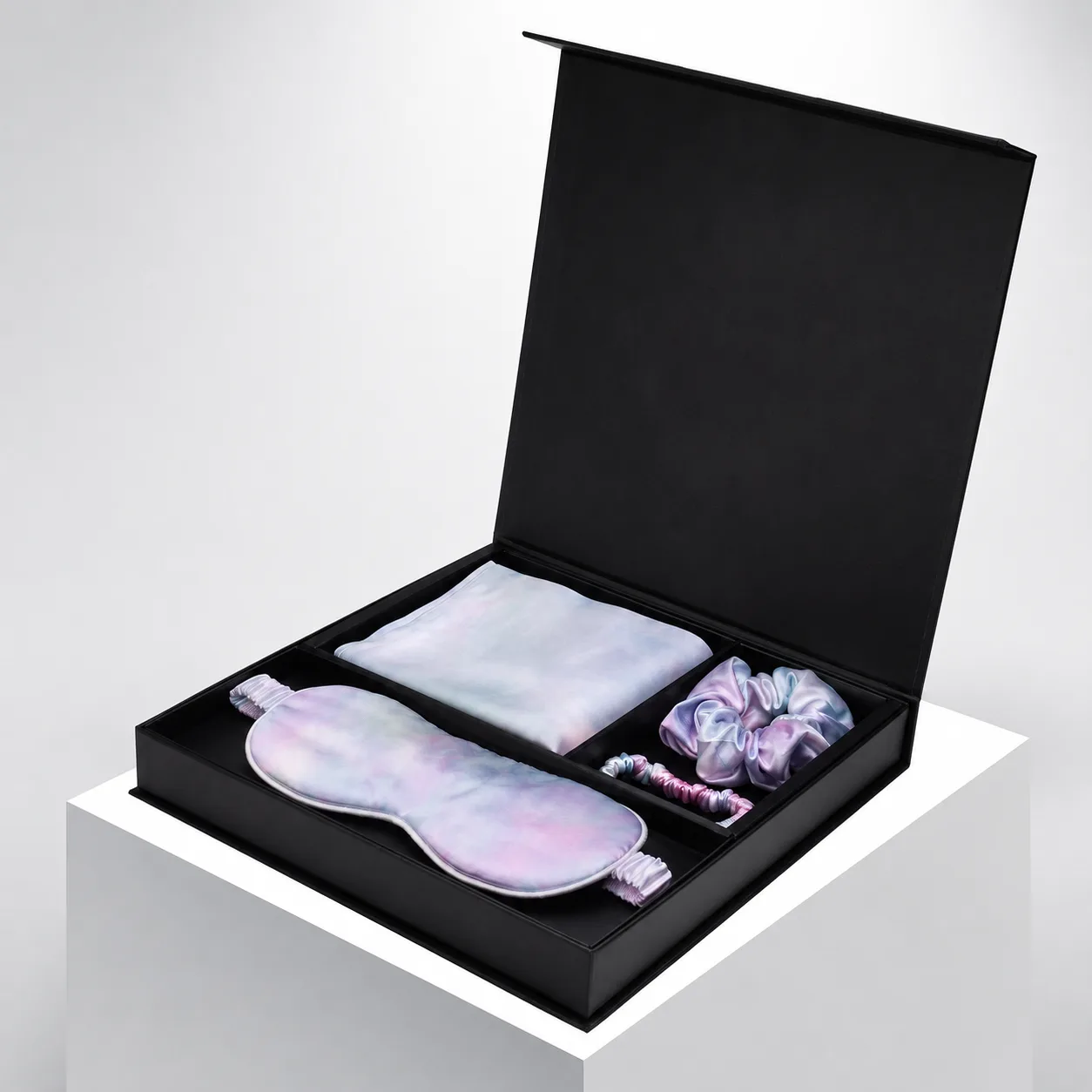 Open black presentation box for a custom silk gift set with pastel sleep mask, pillowcase, and scrunchies for private label beauty and spa programs