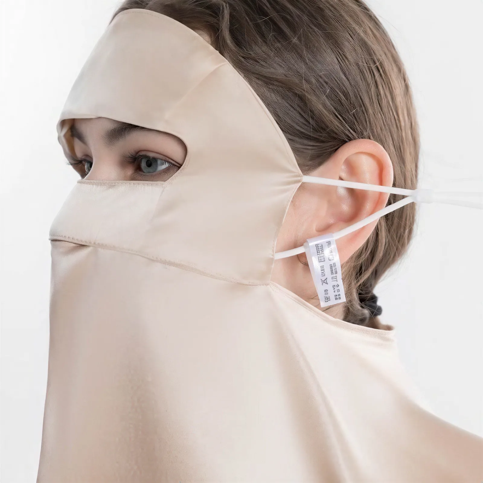 Detail view of custom silk face cover with eye opening, elastic ear loops, and sewn label for private label beauty and travel kits
