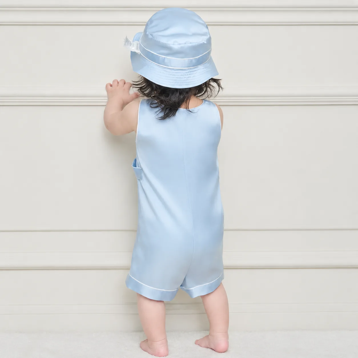 Back detail of custom kids silk romper showing sleeveless relaxed fit, center back seam, bound edges, cuffed leg hems, and structured hat for private