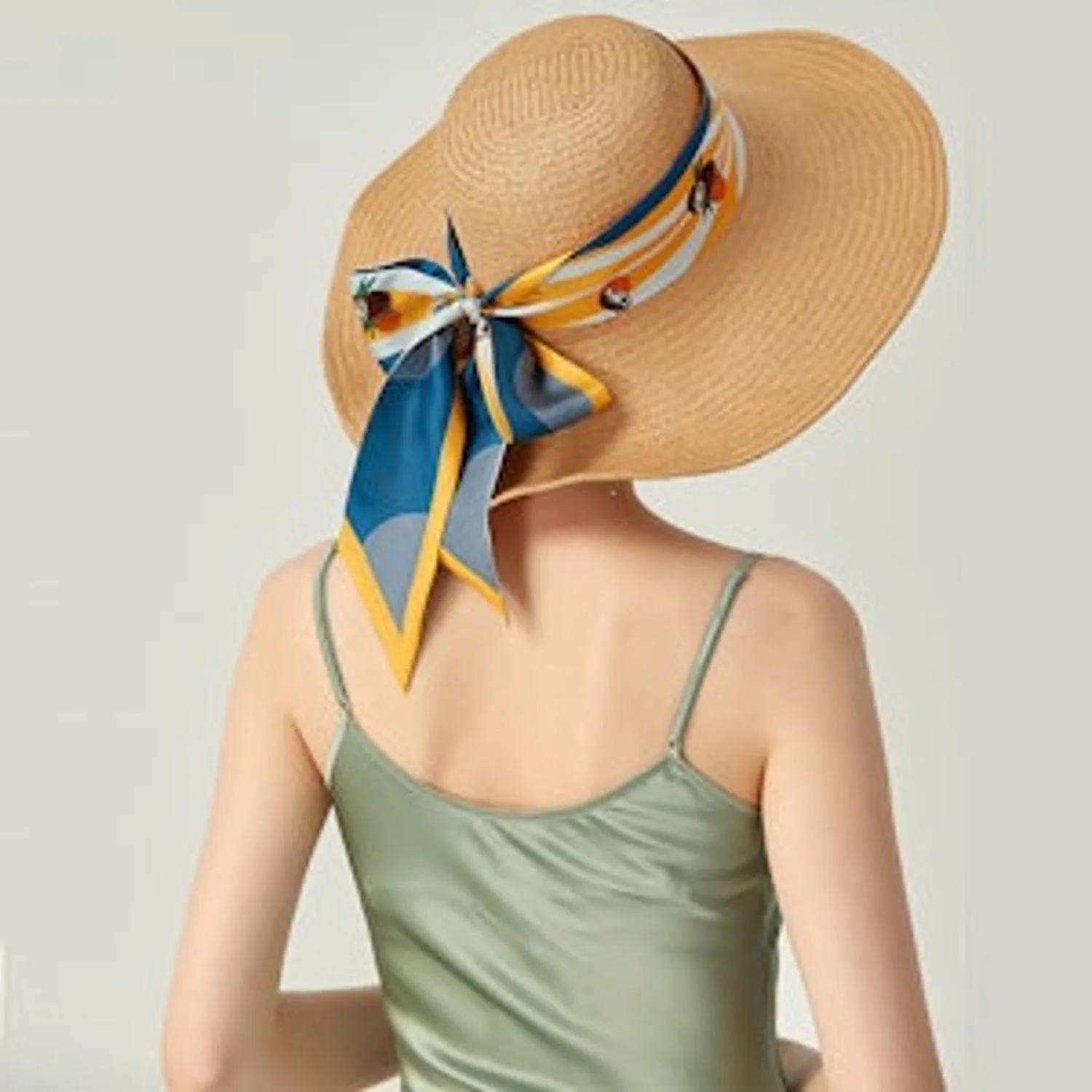 Detail view of a custom silk scarf tied around a straw hat, showcasing the structured design and tailored finish for B2B private label clients