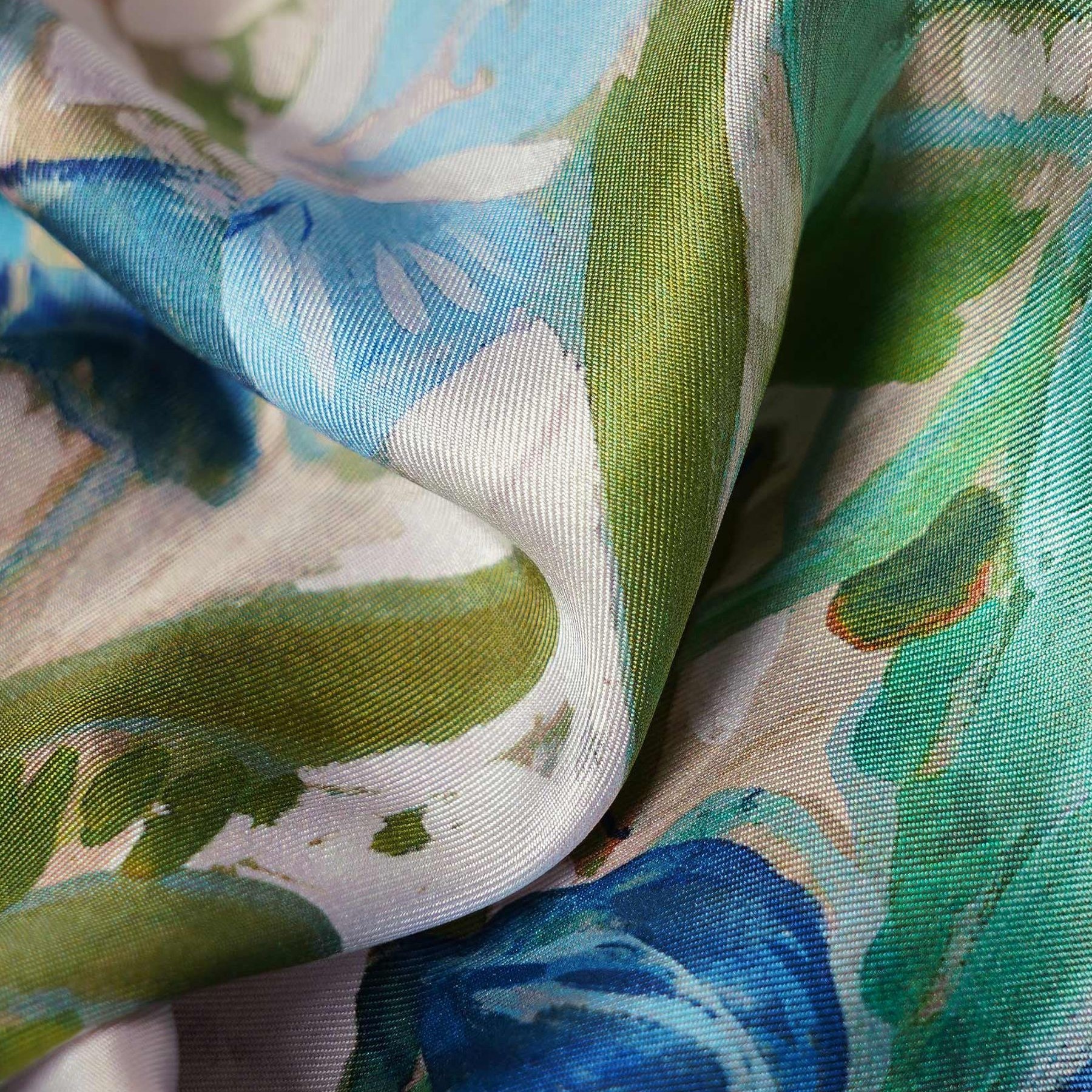 Close-up of a blue and green floral print square silk scarf showing glossy weave, drape, and color detail for private label scarf design review