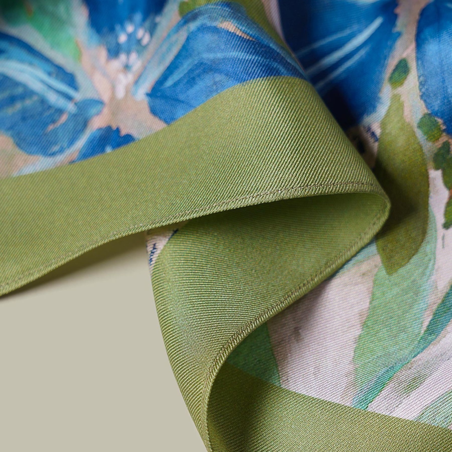 Detail of square custom silk scarf with green border, blue floral print, and finished hem for private label fashion or gift collections